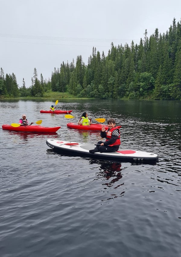 Timur (12 år) stortrives på vannet med SUP-brett, Aliya (10 år), Hussnya (9 år) og Hamiltan (12 år) padler forbi i kajakk.