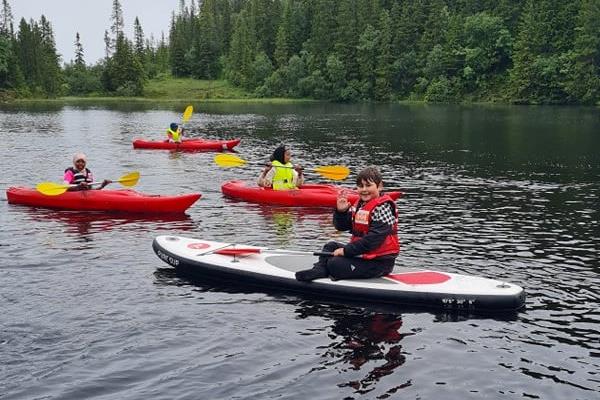 Timur (12 år) stortrives på vannet med SUP-brett, Aliya (10 år), Hussnya (9 år) og Hamiltan (12 år) padler forbi i kajakk.