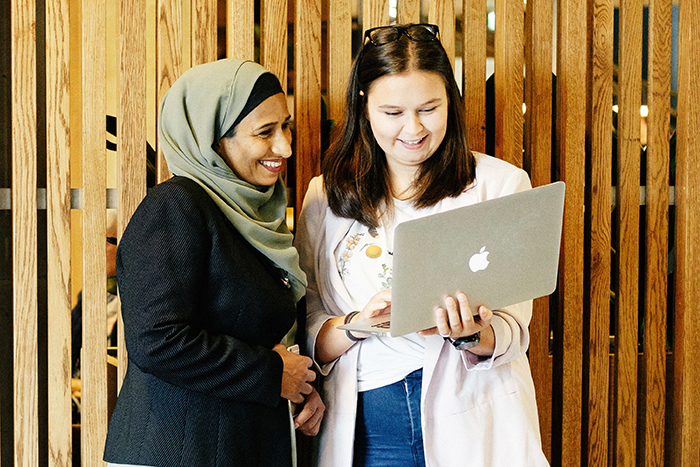 Foto av to kvinner med laptop stående foran en spilevegg